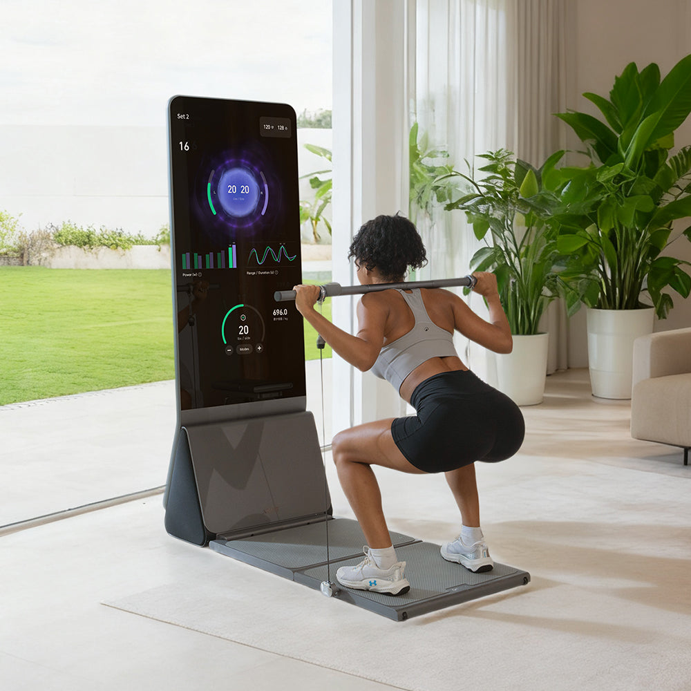 A woman in athletic wear performs a barbell squat while facing a smart fitness mirror that displays real-time workout data in a brightly lit home gym.